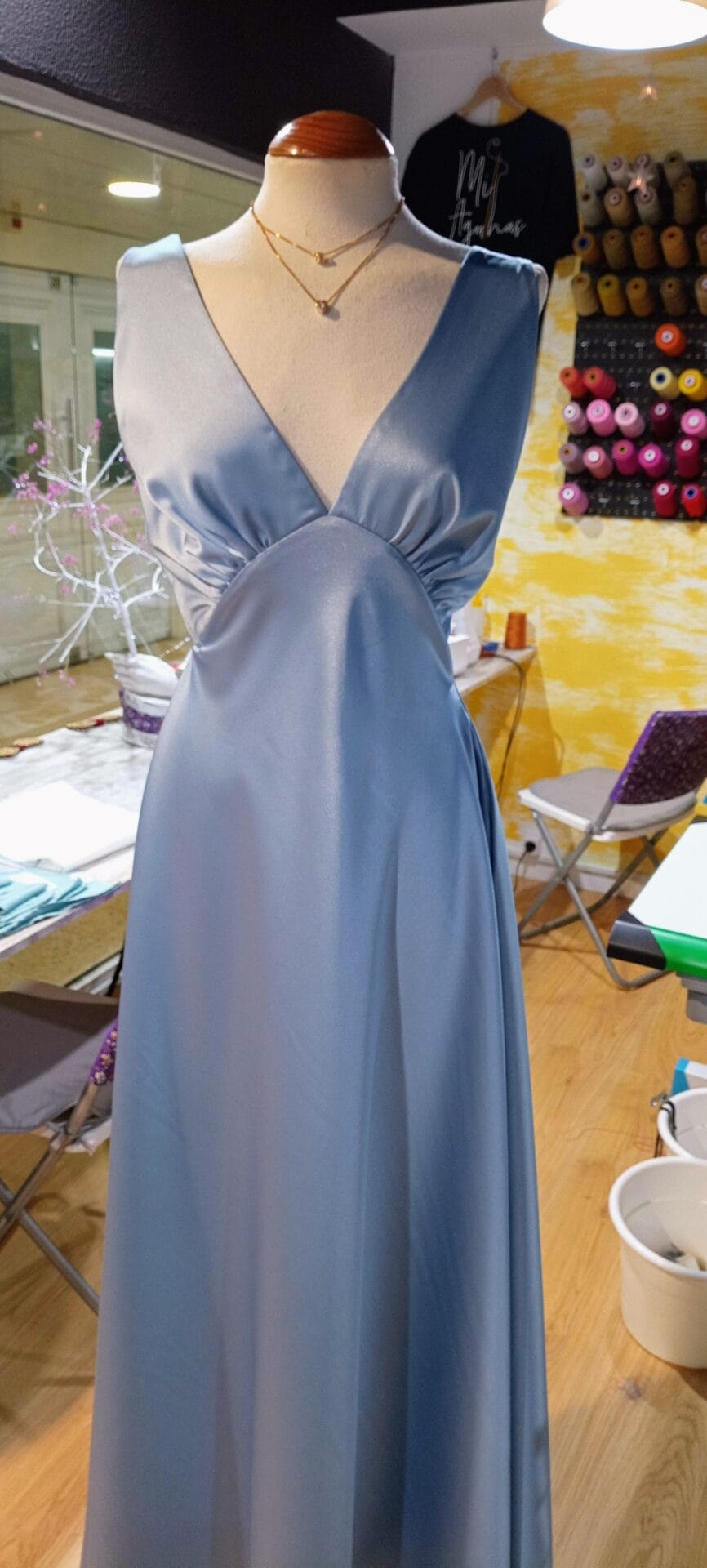 Vestido de festa longo azul serenity em cetim, com decote em V e saia fluida, exposto em manequim no ateliê Mil Agulhas em Coimbra.