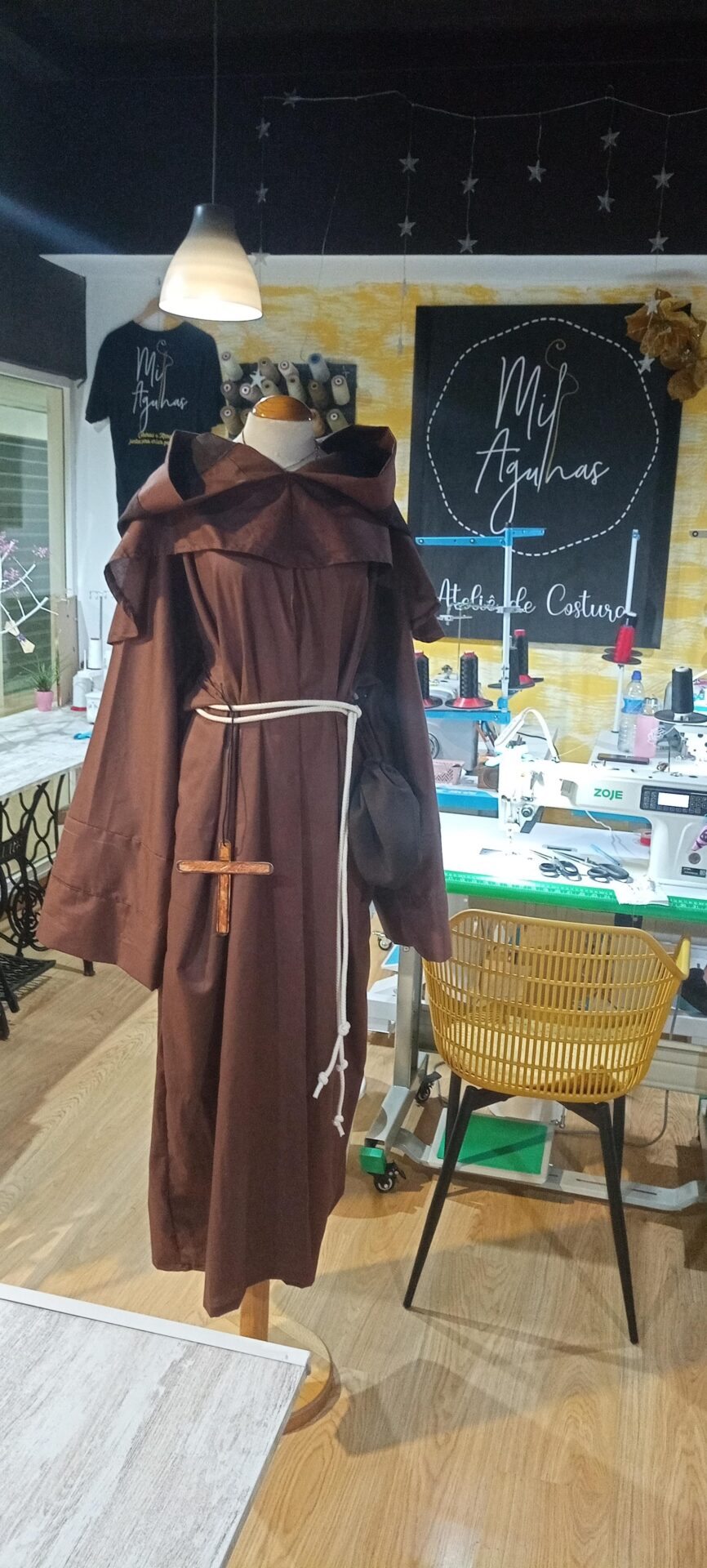 Hábito de monge castanho com capuz e cíngulo branco com crucifixo de madeira, exposto em manequim no ateliê de costura Milagulhas em Coimbra.