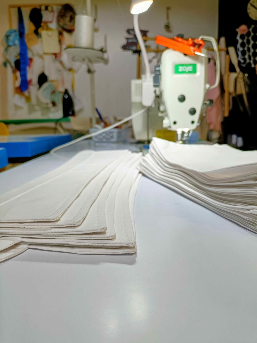 Pilhas de colarinhos e punhos brancos novos ao lado de uma máquina de costura no Ateliê Mil Agulhas, prontos para o serviço de reparação de camisas.