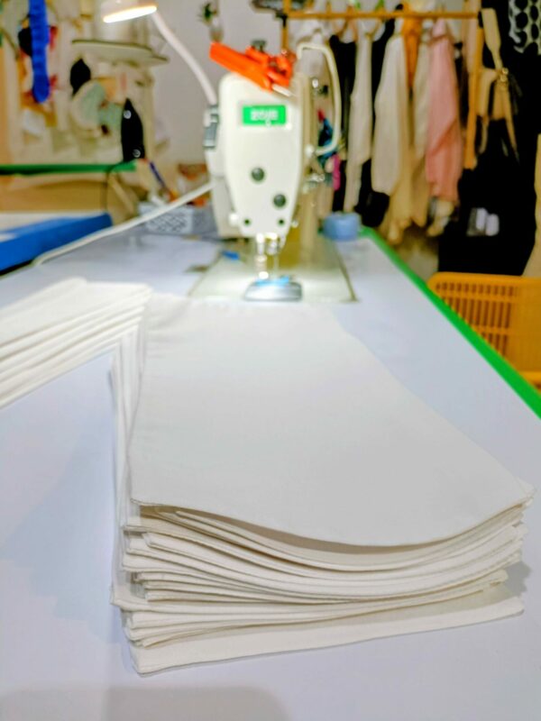 Pilha de punhos de camisa brancos, recém-feitos e alinhados, para o serviço de substituição no ateliê de costura Mil Agulhas.
