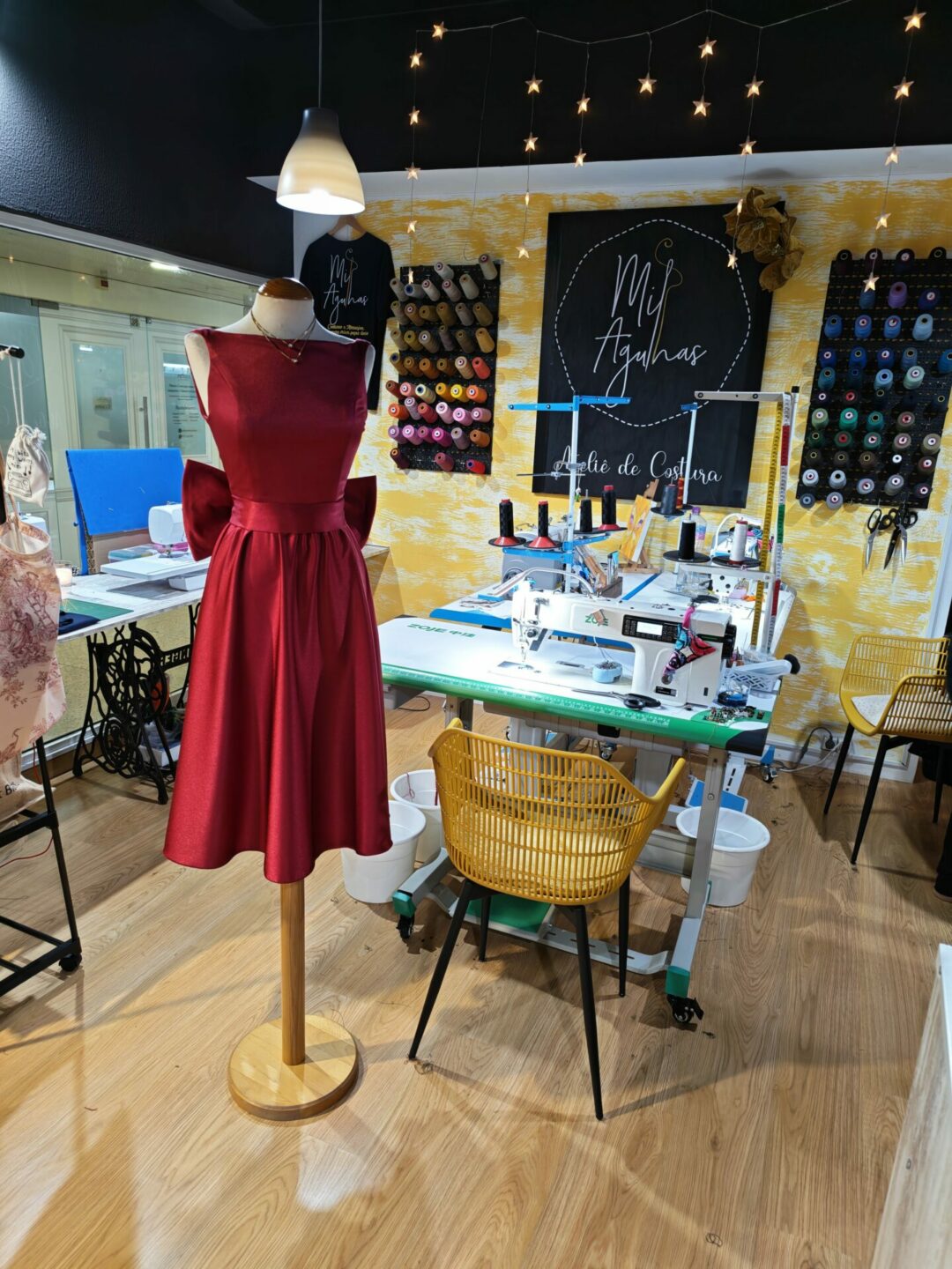 Vista frontal de um elegante vestido de cerimónia vermelho feito à medida, com decote em barco e saia evasê. O vestido está exposto num manequim no ateliê de costura Mil Agulhas.